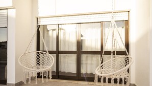 Two white macramé swing chairs hanging from a ceiling, positioned in front of a large window with curtains. - Ericeira Paradise House & Suites (Mafra)