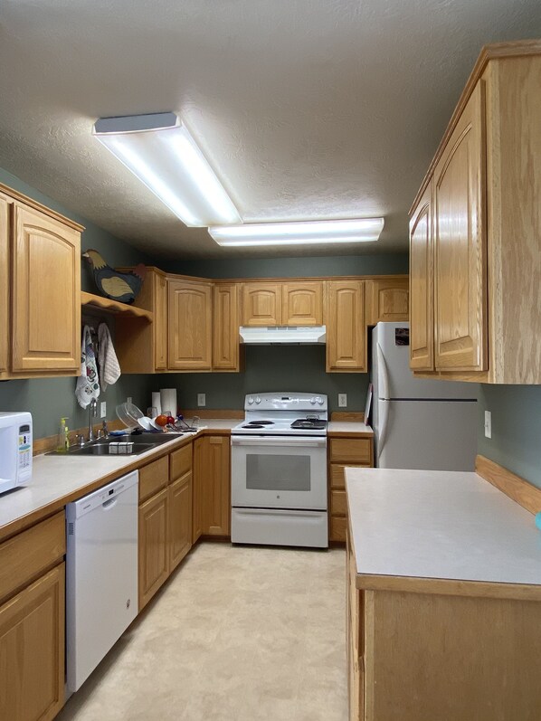 A kitchen with wooden cabinets, a white stove, a refrigerator, and a dishwasher. - Two Bit Ranch House (Escalante)