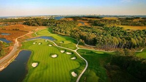 Vista aérea de un campo de golf con múltiples búnkeres, obstáculos acuáticos y un área boscosa circundante.