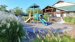 Un parque infantil con un tobogán y estructuras para escalar, un pabellón y un edificio con techo verde.