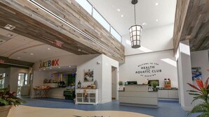 Un interior moderno con un mostrador de recepción, una barra JuiceBox y un cartel de bienvenida al Health Aquatic Club en Bayside.