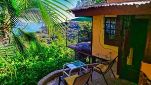 Un balcón con mesa y sillas, con vista a un paisaje verde y exuberante y una masa de agua.