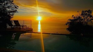 Atardecer sobre un cuerpo de agua tranquilo, con piscina y sillas de descanso.