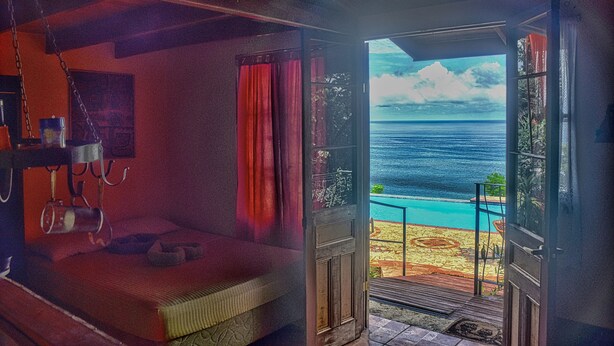 Una habitación con cama, una mesita y vista al océano a través de una puerta abierta.