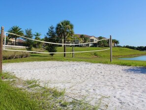 Een zandstrand met een volleybalnet, palmbomen en een huis op de achtergrond.
