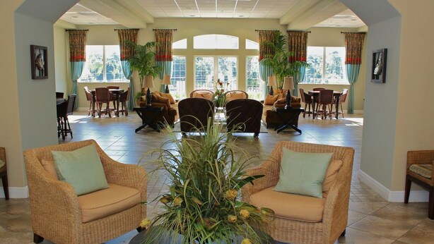 A spacious lobby with wicker furniture, a central black coffee table, and large windows with curtains.