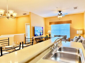 A modern kitchen with a central island, a dining area with chairs, a television, and a ceiling fan.