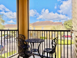A balcony with a view of a residential area, featuring a yellow building, a red car, and a clear sky.