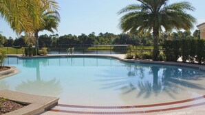 A swimming pool with a curved edge, surrounded by palm trees and a fence.