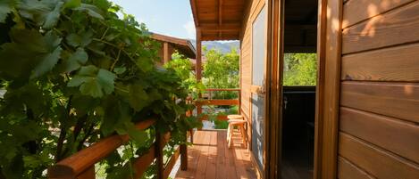 A wooden deck with a pergola, a hanging light fixture, and a view of greenery and mountains in the background.