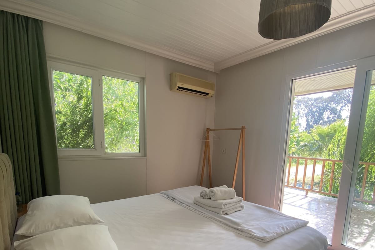 Un letto rifatto con lenzuola bianche, un lampadario a sospensione e vista sul verde circostante.
