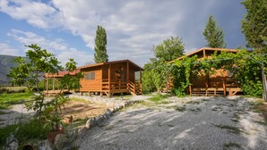 Two wooden cabins with wooden decks, surrounded by greenery and a gravel path. - Bhavana Gokova (Ula)