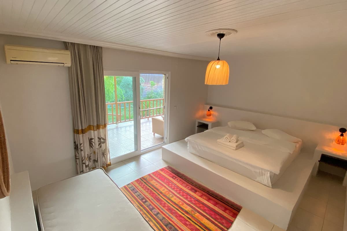 Camera d'albergo con un letto, un comodino, tende a una finestra, un condizionatore d'aria e vista sull'esterno.