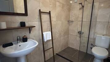 Een badkamer met een wastafel op een zuil, een spiegel, een douchecabine en een toilet.