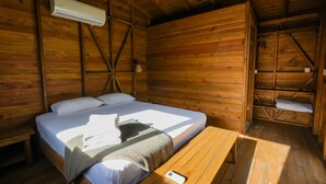 A wooden cabin room with a bed, a bench, and an air conditioning unit. - Bhavana Gokova (Ula)