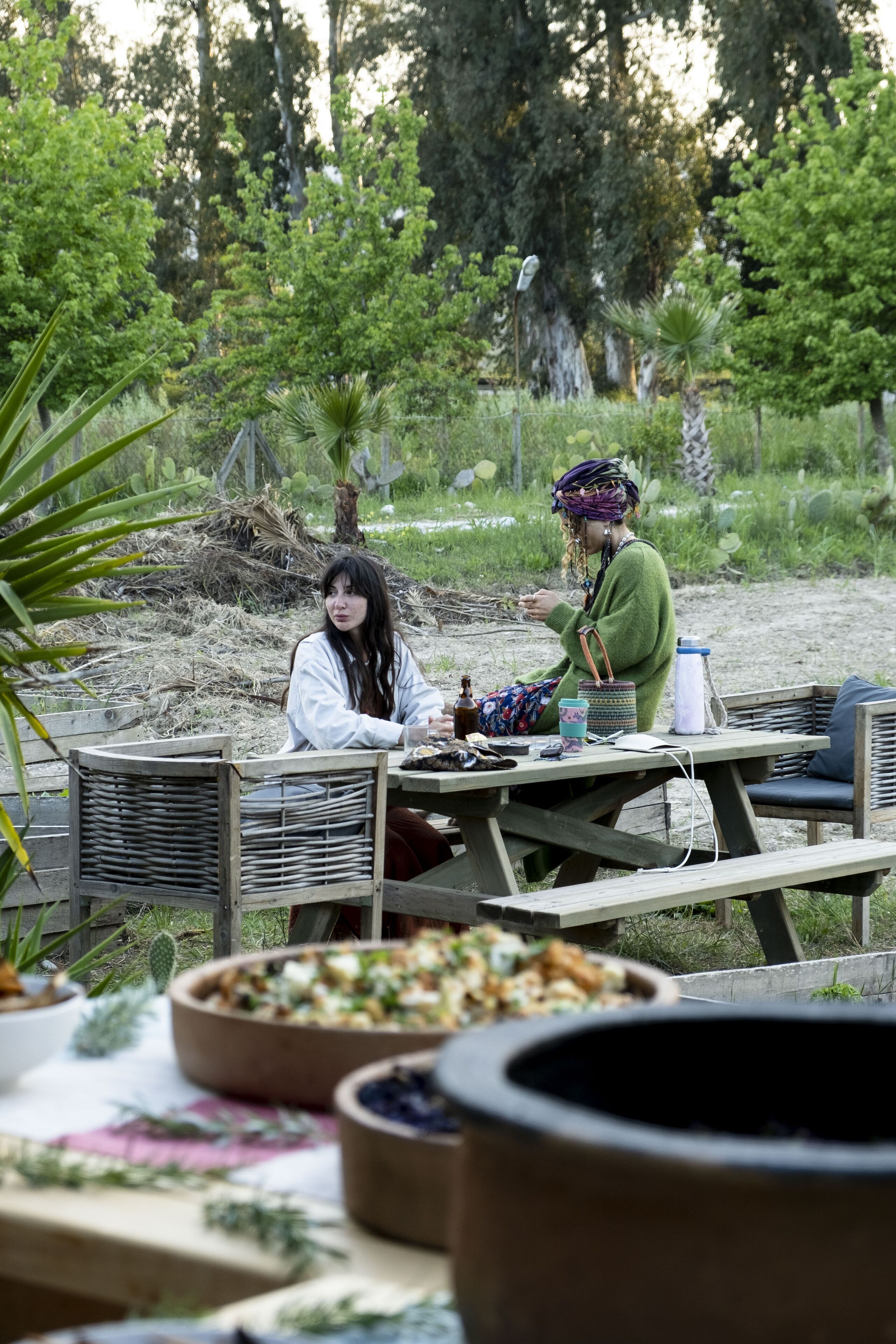 Un coin repas avec une table en bois dressée pour deux personnes, entouré de plantes en pot et d’un décor rustique.