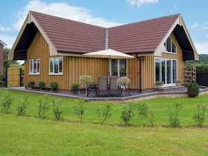A two-story wooden house with a sloped roof, a covered patio with outdoor furniture, and a well-maintained lawn.