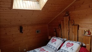 A cozy wooden cabin bedroom with a skylight, a bed with heart-patterned bedding, and a wooden headboard. - Gîte la grange de l'errance (Giron)