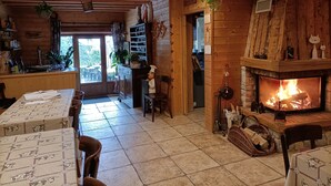 A cozy cabin interior with a fireplace, wooden walls, and a dining area with tables set for two. - Gîte la grange de l'errance (Giron)