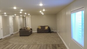 A spacious living room with hardwood flooring, two sofas, a ceiling light fixture, and a window with blinds. - Spacious Suite: Basement Apartment (Enoch)