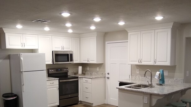 A modern kitchen with white cabinets, stainless steel appliances, and a wooden floor. - Spacious Suite: Basement Apartment (Enoch)