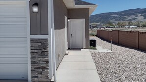 A building with a garage door, a stone accent wall, and a clear view of a mountainous landscape. - Spacious Suite: Basement Apartment (Enoch)