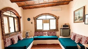 A room with a central bed, two side beds, a wooden ceiling, a tiled floor, and a window with a view.