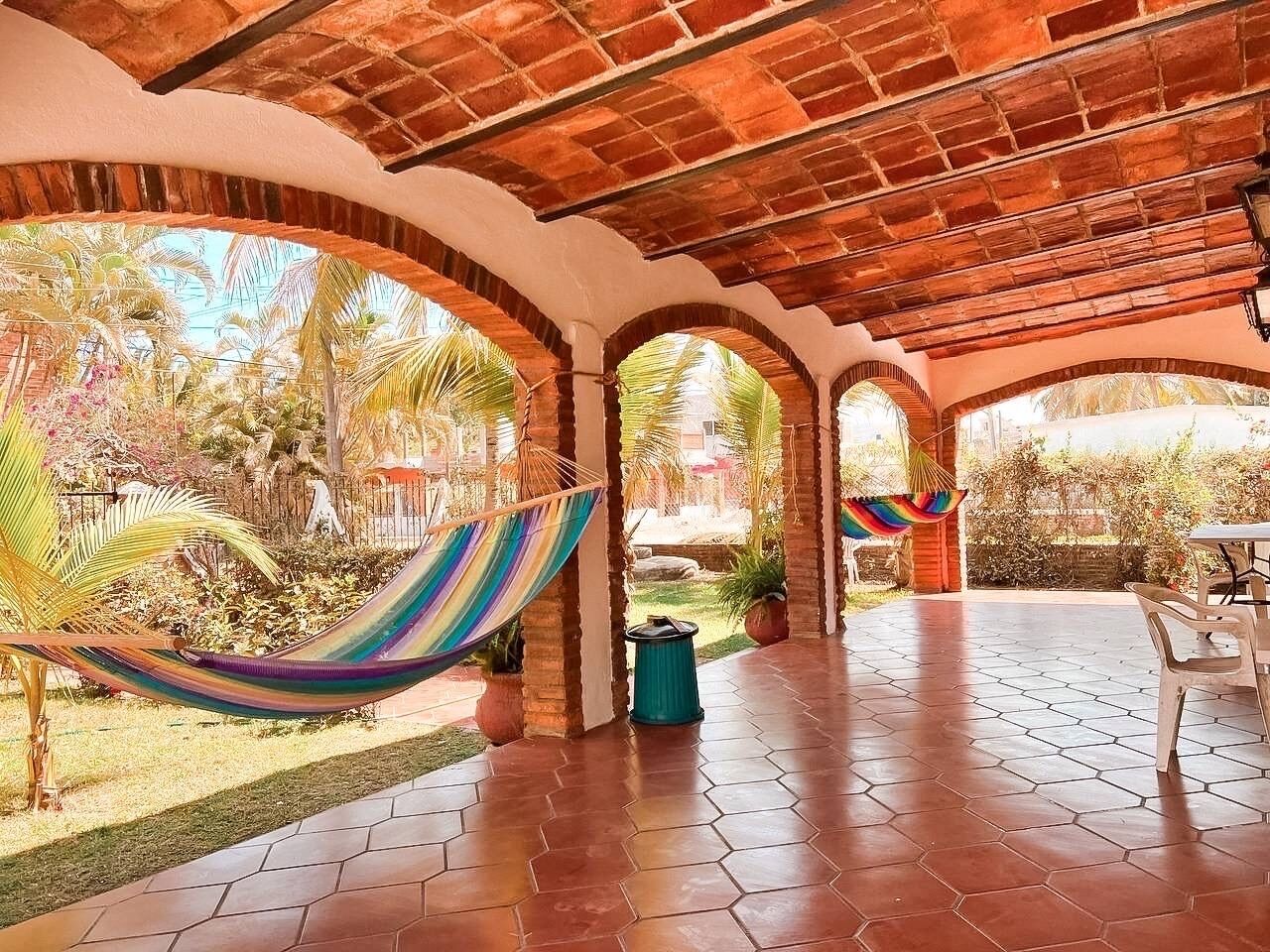 A covered patio area with hexagonal tiled flooring, a hammock, and a table with chairs.