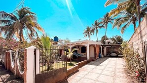 A paved pathway leading to a gated entrance with a water tank and palm trees.