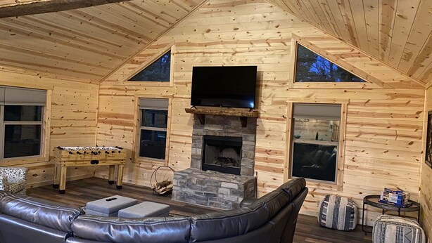 A cozy log cabin interior with a stone fireplace, leather sofa, and a television mounted above it.
