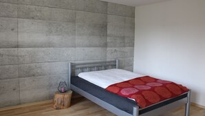 A modern bedroom with a metal bed frame, a grey headboard, a wooden stool, and a red patterned blanket.