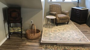 A room with a patterned rug, a chair, a small table, a wicker basket, a dark wooden cabinet, and a window with decorative items. - Explore Pittsburgh from a Modern, Hip Bungalow (Pittsburgh)