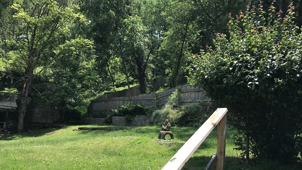 A grassy outdoor area with a wooden bench, a stone statue, and a wooden fence. - Explore Pittsburgh from a Modern, Hip Bungalow (Pittsburgh)