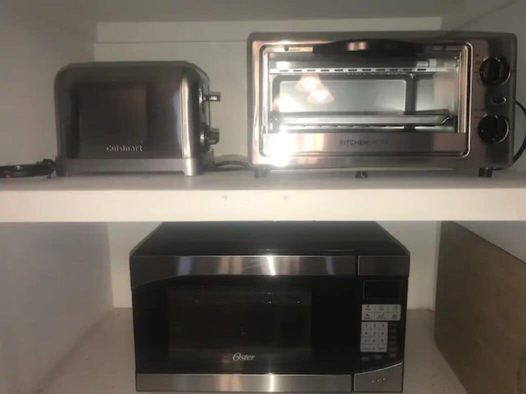 A kitchen with a toaster, a toaster oven, and a microwave on a shelf.