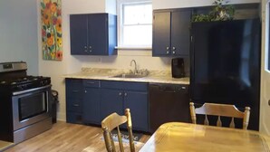 A kitchen with dark blue cabinets, a black refrigerator, a stove, and a dining table with chairs. - Explore Pittsburgh from a Modern, Hip Bungalow (Pittsburgh)