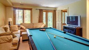 Une table de billard dans une pièce où se trouvent un canapé et un téléviseur.