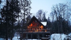 Une cabane en rondins dotée d’un balcon, entourée de neige et d’arbres.