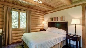 Une chambre à coucher dans une cabane en bois, avec un lit, deux lampes de chevet et une fenêtre avec des rideaux.
