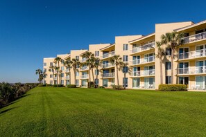Ein mehrstöckiges Hotel mit Balkonen, Palmen und einem gepflegten Rasen.
