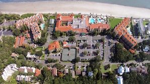 Luftaufnahme eines Küstenresorts mit mehreren Gebäuden, einem Tennisplatz und einem Strand.