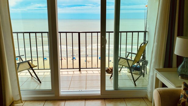 Une pièce dotée d’une porte-fenêtre coulissante donnant sur un balcon avec vue sur la plage.