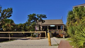 A beach volleyball court with a net, a wooden fence, and a building with a porch in the background. - Beach Access Villa with Indoor & Outdoor Pools - Private Balcony - Updated (Hilton Head Island)