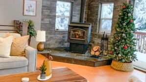 A cozy living room with a stone fireplace, a Christmas tree, and a comfortable sofa. - Jeremys Mountain Chalet @jeremysmountainchalet (Anchorage)