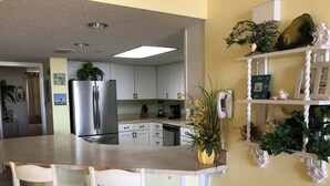 Una cucina con mobili bianchi, un frigorifero in acciaio inox, un'isola integrata con sedie e piante ornamentali.
