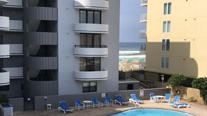 Una piscina con lettini, vista sull'oceano e un edificio a più piani con balconi.