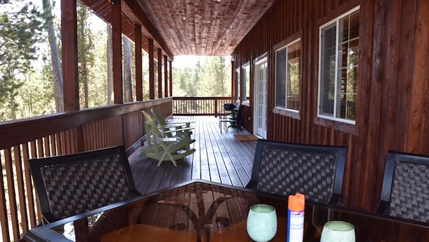 A wooden deck with a glass table and chairs, surrounded by tall trees. - Eagle's Landing, is located in Island Park, ID, 35 miles from West Yellowstone (Island Park)