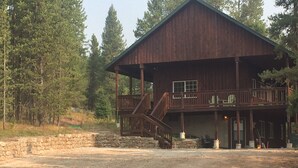 A two-story wooden cabin with a balcony, surrounded by trees. - Eagle's Landing, is located in Island Park, ID, 35 miles from West Yellowstone (Island Park)