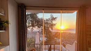Een balkon met een bank en een tafel, met uitzicht op een prachtig landschap van bomen en een zonsondergang.
