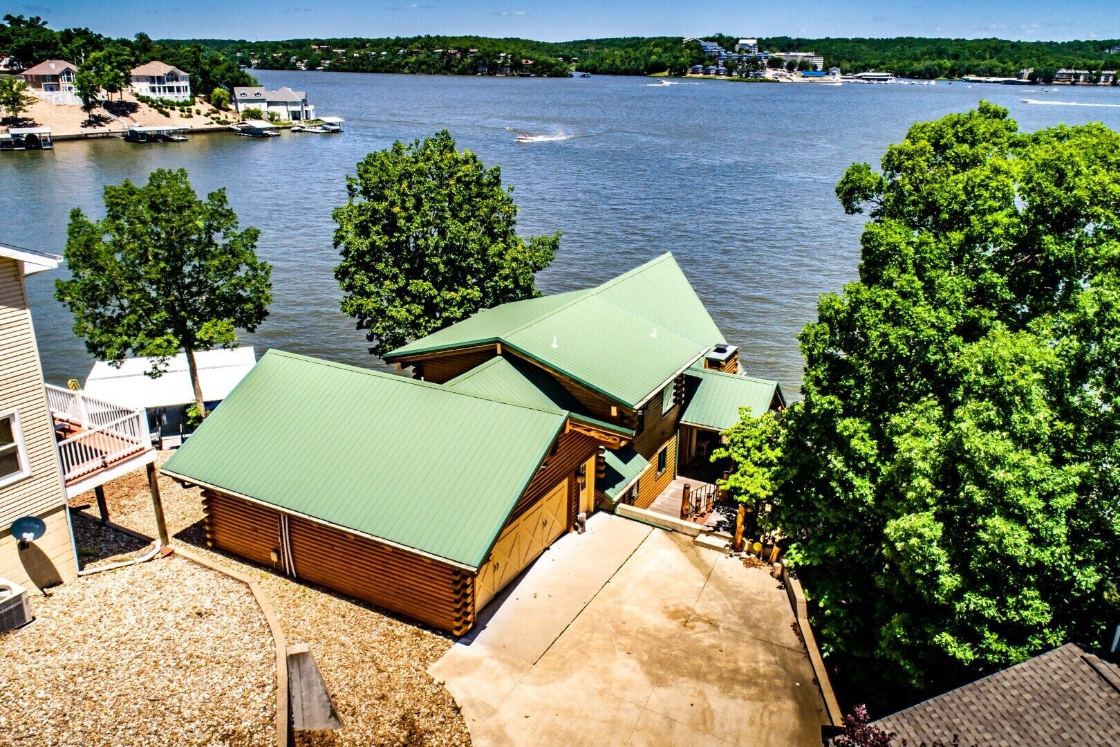 Uma cabana à beira do lago com telhado verde, rodeada por árvores e uma vista desobstruída do lago.