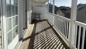 A covered wooden deck with white railings, a table, and a chair.